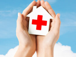 hands holding paper house with red cross